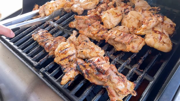 A close-up image capturing the process of grilling marinated chicken pieces, with a person expertly flipping them to ensure even cooking on a classic outdoor barbecue grill.