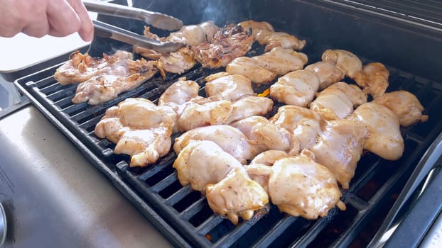 A close-up image capturing the process of grilling marinated chicken pieces, with a person expertly flipping them to ensure even cooking on a classic outdoor barbecue grill.