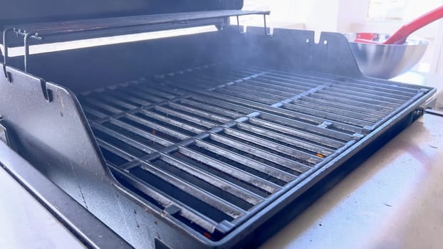 A hand uses a red grill brush to clean the black grates of a barbecue grill, ensuring it remains in perfect condition for the next grilling session.