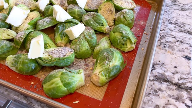 Fresh Brussels sprouts seasoned with spices and topped with slices of butter, arranged on a baking sheet, ready to be roasted to perfection.