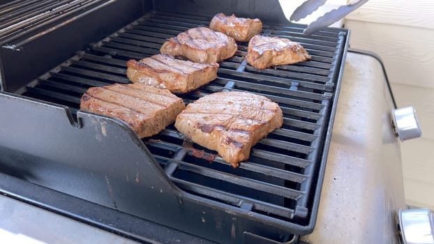 Several thick steaks with grill marks cooking to perfection on an outdoor grill, capturing the essence of a sunny barbecue day.