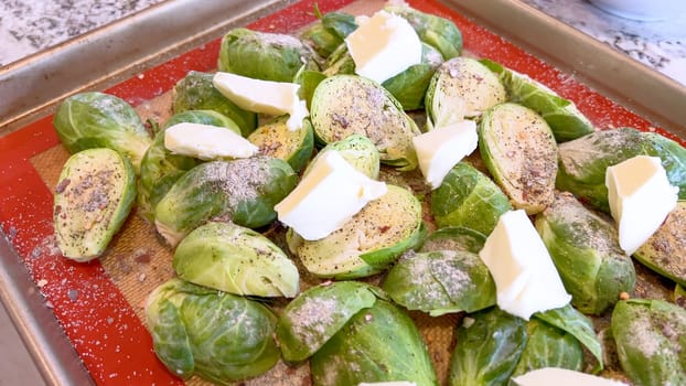 Fresh Brussels sprouts seasoned with spices and topped with slices of butter, arranged on a baking sheet, ready to be roasted to perfection.