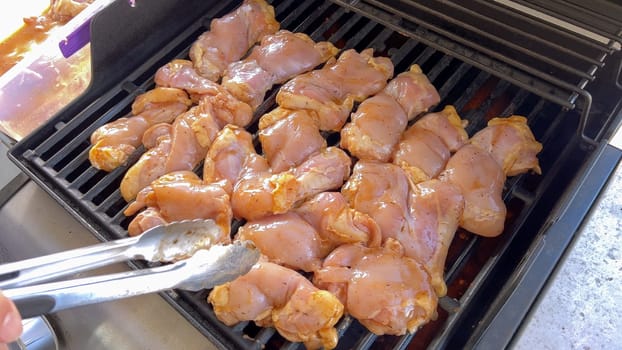 A close-up image capturing the process of grilling marinated chicken pieces, with a person expertly flipping them to ensure even cooking on a classic outdoor barbecue grill.