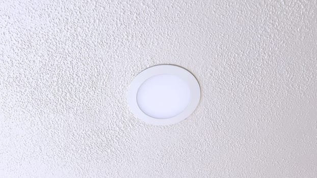 A simple and modern ceiling light fixture is centrally positioned against a textured white ceiling, providing clean and efficient illumination within a room.
