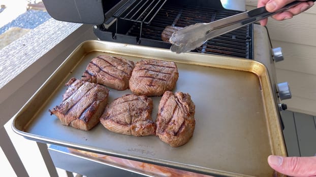 Several thick steaks with grill marks cooking to perfection on an outdoor grill, capturing the essence of a sunny barbecue day.