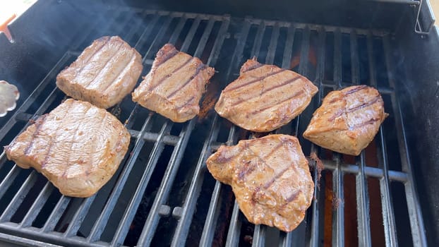 Several thick steaks with grill marks cooking to perfection on an outdoor grill, capturing the essence of a sunny barbecue day.