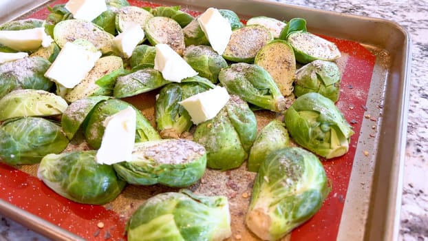 Fresh Brussels sprouts seasoned with spices and topped with slices of butter, arranged on a baking sheet, ready to be roasted to perfection.