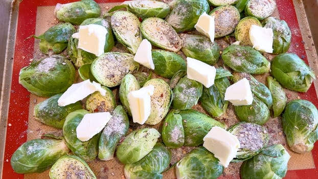 Fresh Brussels sprouts seasoned with spices and topped with slices of butter, arranged on a baking sheet, ready to be roasted to perfection.