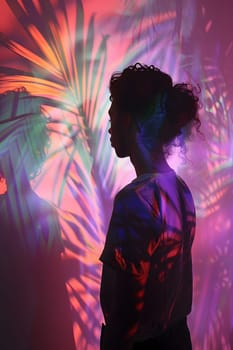 A woman is illuminated in electric blue and pink lighting while standing in front of a projection of leaves, creating a visually stunning art display