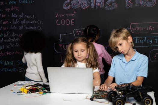 Smart girl in white bib learning about coding robotics technology using laptop in the STEM class. Schoolboy in blue shirt try to educate motherboard while smart schoolgirls reading code. Erudition.