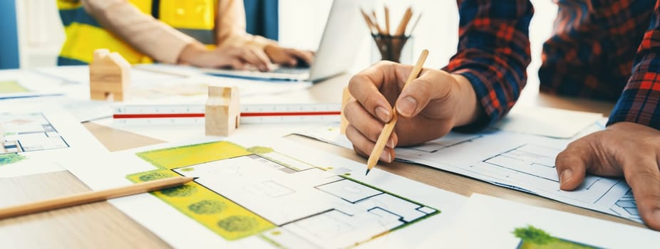 A cropped portrait of professional architect working with blueprint during safety engineer using laptop analysis data at meeting table with document scatter around. Close up. Delineation.