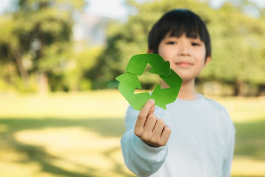 Cheerful young asian boy holding recycle symbol on daylight natural green park promoting waste recycle, reduce, and reuse encouragement for eco sustainable awareness for future generation. Gyre