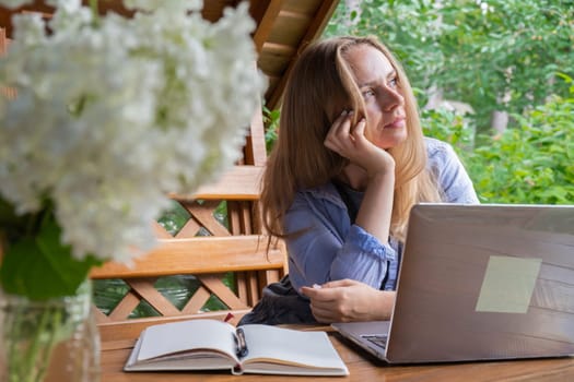 Young happy woman focuses on her laptop in wooden alcove. Relaxed outdoor setting emphasizes comfort and productivity. Remote work learning concept