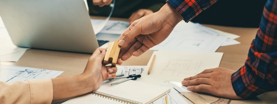 Professional architect team discussion about architectural project on meeting table with blueprint and wooden block scatter around at modern office. Closeup. Focus on hand. Delineation.