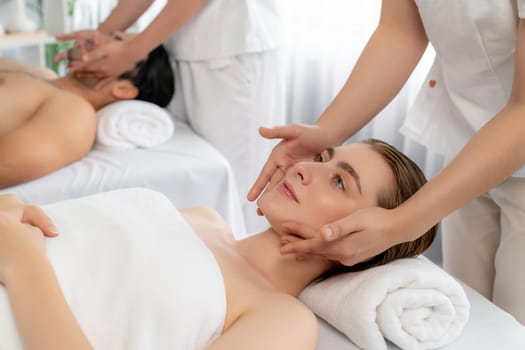 Caucasian couple enjoying relaxing anti-stress head massage and pampering facial beauty skin recreation leisure in dayspa modern light ambient at luxury resort or hotel spa salon. Quiescent