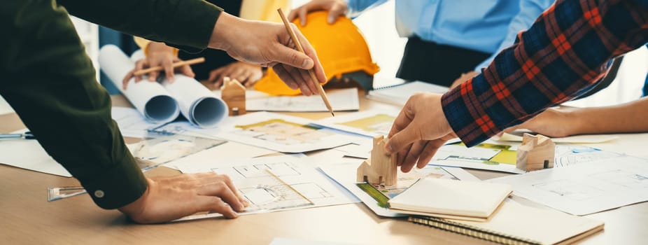 Professional architect team and safety engineer with safety helmet brainstorming about architectural project on meeting table with blueprint scatter around. Close up. Focus on hand. Delineation.