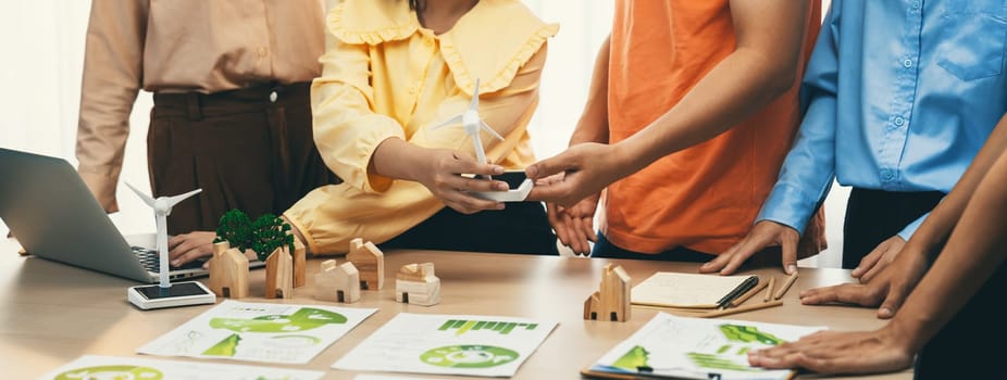 Windmill model represented using renewable energy placed during presenting green business on table with wooden block and environmental document scatter around. Closeup. Delineation.