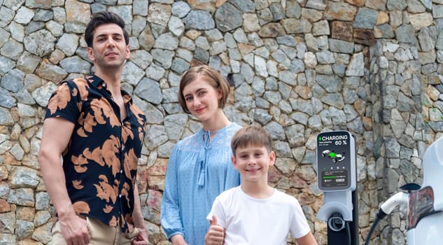 Family road trip vacation with electric vehicle, lovely family recharge EV car with green and clean energy. Stone seawall background and eco friendly car travel for sustainable environment. Perpetual