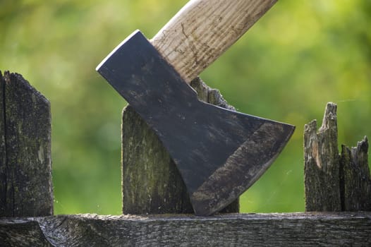 Close up of an axe with brown handle and dark grey blade embedded in an aged, cracked wooden fence post