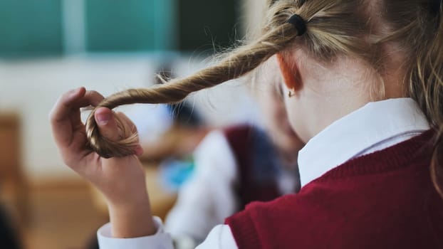 A girl touches a braid of her hair during class