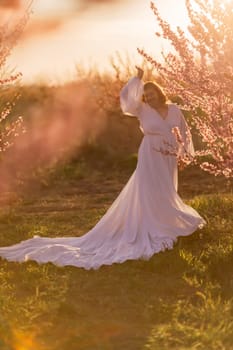 Woman blooming peach orchard. Against the backdrop of a picturesque peach orchard, a woman in a long white dress enjoys a peaceful walk in the park, surrounded by the beauty of nature