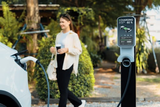 Young woman and sustainable urban commute with EV electric car recharging at outdoor cafe in springtime garden, green city sustainability and environmental friendly EV car. Expedient