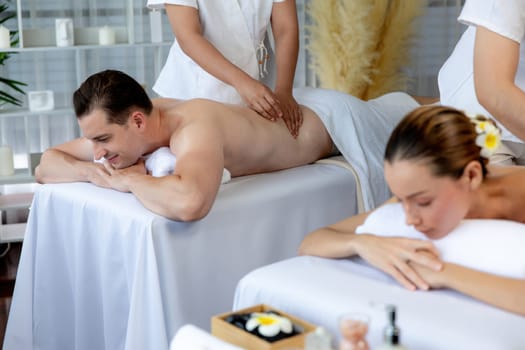 Caucasian couple customer enjoying relaxing anti-stress spa massage and pampering with beauty skin recreation leisure in day light ambient salon spa at luxury resort or hotel. Quiescent