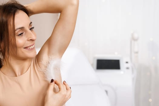 Armpit epilation, hair removal. Young woman holding her hands up and showing clean armpits, depilating smooth transparent skin. Portrait of beauty. Armpit care. Large white feather near the skin