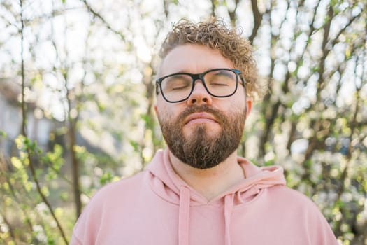 Man with beard and mustache on smiling face near sakura flowers or blooming spring tree. Soft and gentle concept. Bearded man with stylish haircut with flowers on background, close up. Hipster near branch of bloom tree