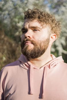 Man with beard and mustache on smiling face near sakura flowers or blooming spring tree. Soft and gentle concept. Bearded man with stylish haircut with flowers on background, close up. Hipster near branch of bloom tree