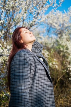 Beautiful red-haired woman enjoying smell in a flowering blooming spring garden. Spring blossom
