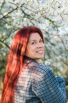 Beautiful red-haired woman enjoying smell in a flowering blooming spring garden. Spring blossom.