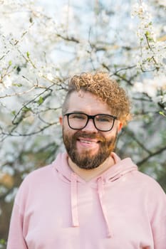 Man with beard and mustache on smiling face near sakura flowers or blooming spring tree. Soft and gentle concept. Bearded man with stylish haircut with flowers on background, close up. Hipster near branch of bloom tree