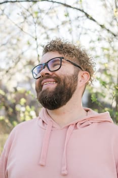 Man with beard and mustache on smiling face near sakura flowers or blooming spring tree. Soft and gentle concept. Bearded man with stylish haircut with flowers on background, close up. Hipster near branch of bloom tree