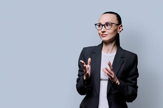 Portrait of thinking serious 30s business woman on grey studio background. Confident female in glasses suit looking to side at space for image text copy space. Business work teaching job career people