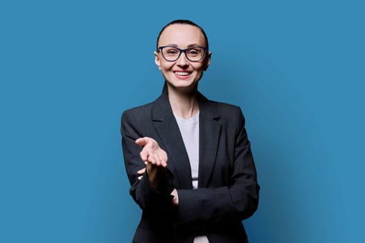 Talking friendly business middle aged elegant woman looking at camera on blue studio background. Business work job career people concept