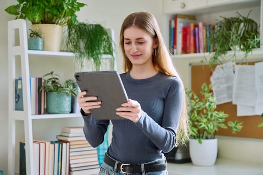 Young teenage female using digital tablet, home interior. Modern wireless technologies, Internet, online, apps applications, digital gadgets