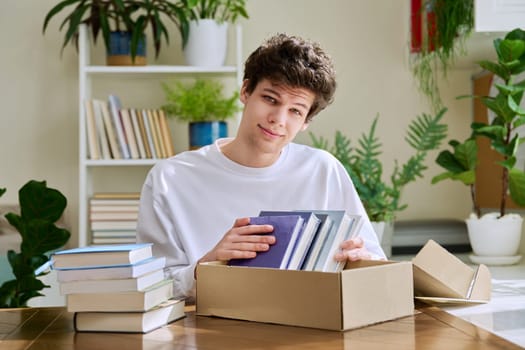 Satisfied young male customer buyer sitting at home unpacking cardboard box parcel with new books, online purchases. Delivery by mail, internet store bookstore