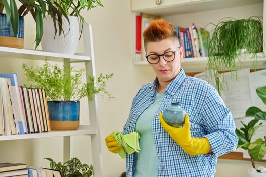 Middle-aged woman cleaning house, female wiping dust in room. Housekeeping, housework, housecleaning, cleaning concept