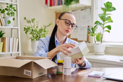 Satisfied female customer buyer sitting at home unpacking cardboard box with online purchases. Woman unpacking boxes with cosmetics care products vitamins perfumes. Delivery by mail, online store