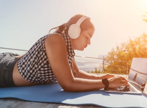 Digital nomad, Business woman working on laptop by the sea. Pretty lady typing on computer by the sea at sunset, makes a business transaction online from a distance. Freelance, remote work on vacation