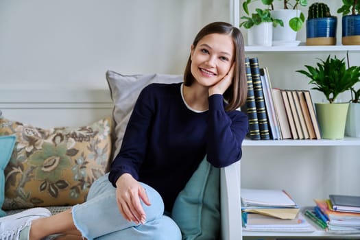 Portrait of young attractive smiling woman in home interior. Happy cheerful relaxed 20s female looking at camera, sitting on couch. Beauty, youth, happiness, health, lifestyle concept