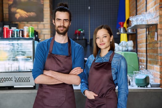 Small business team portrait of confident successful colleagues partners young man woman in aprons posing looking at camera at workplace in restaurant coffee shop cafeteria. Partnership teamwork work