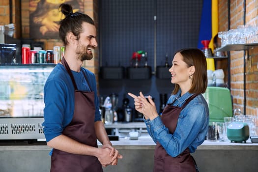 Small business team, successful colleagues partners workers young man and woman in aprons talking at workplace in restaurant coffee shop cafeteria. Cooperation, partnership, teamwork, staff, work