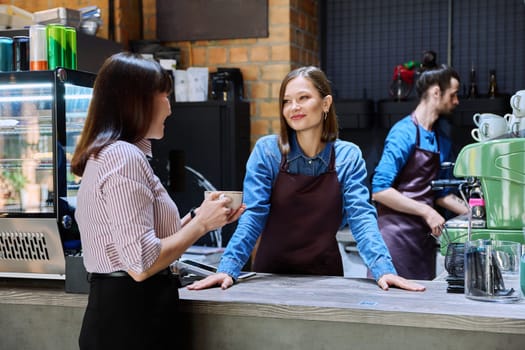 Woman customer of coffee shop near counter with cup of coffee talking to restaurant workers owners. Workplace at bar, colleagues, partners in food service, work, entrepreneurship, small business