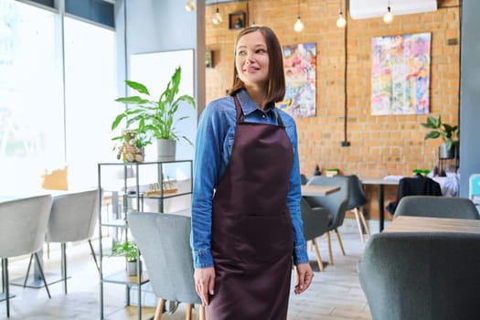 Attractive successful young woman service worker, business owner in apron in restaurant cafeteria coffee pastry shop interior. Small business staff occupation entrepreneur work