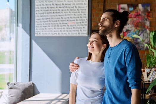 Young happy couple hugging together looking out the window. Love, friendship, romance, relationship, happiness, lifestyle, people concept