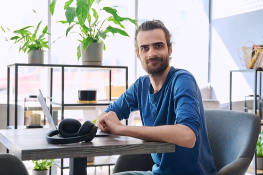 Portrait of young handsome smiling man freelancer entrepreneur working with laptop computer, looking at camera, sitting at table in coworking cafe. Business, work, education, study, freelance, 30s guy