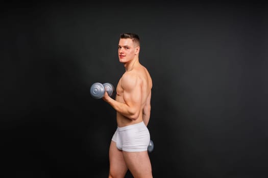 Man with pumped-up body with dumbbells in his hands white panties exercise