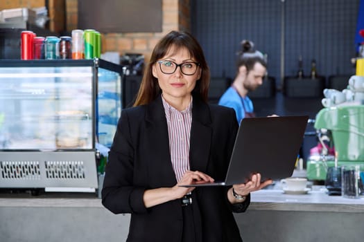 Portrait of confident business woman accountant financier lawyer small business owner. Successful middle-aged female using laptop computer looking at camera background coffee shop cafeteria restaurant